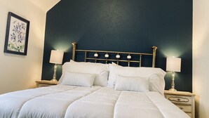 A neatly made bed with white bedding, two bedside tables with lamps, and a dark blue wall. - The Heart of Fraser (Fraser)