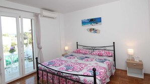A bedroom with a bed, a nightstand, a window with curtains, and a wall-mounted air conditioner. - GABRIEL One-Bedroom Apartment 3 (Rovinj)