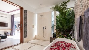 Une salle de bain moderne avec une baignoire sur pieds remplie de pétales de roses, un espace douche et une grande plante en pot.