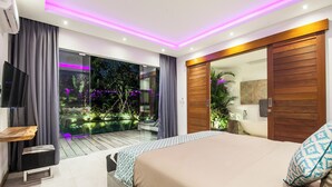 Une chambre moderne avec un grand lit, une télévision et une porte-fenêtre coulissante donnant sur un balcon agrémenté de plantes et offrant une vue agréable.