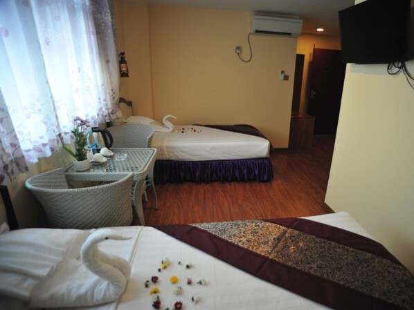 A hotel room with two beds, a small table with chairs, a potted plant, and a wall-mounted TV.