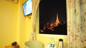 A room with a view of the Eiffel Tower at night, a television on the wall, a table with a kettle and bottles, and a chair. - Hotel Lavender (Yangon)