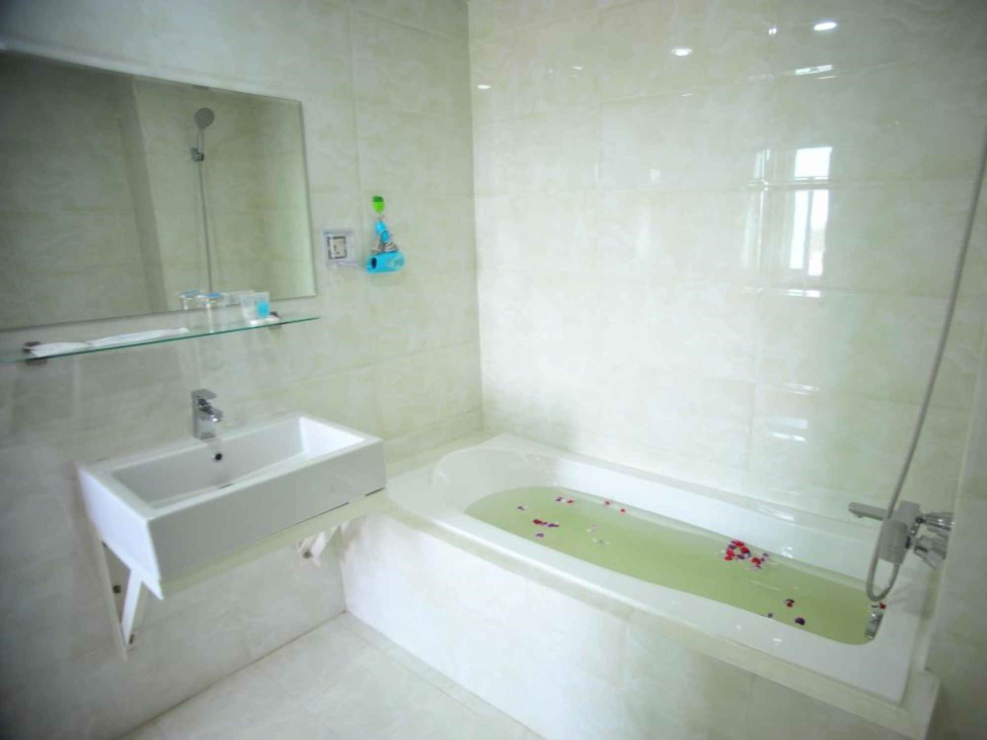 A modern bathroom with a white sink, a glass shelf, a bathtub with flowers, and a shower.