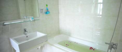 A modern bathroom with a white sink, a glass shelf, a bathtub with flowers, and a shower.