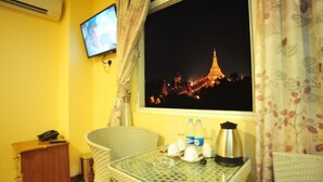 A room with a view of a lit-up pagoda at night, a television on the wall, a table with a kettle, bottles, and glasses. - Hotel Lavender (Yangon)
