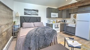 A compact bedroom with a bed, bedside table, and a wall-mounted clock. Adjacent is a kitchenette with a microwave, stove, and refrigerator. - A Night with the Alpacas & Alpaca Experience! (Silt)