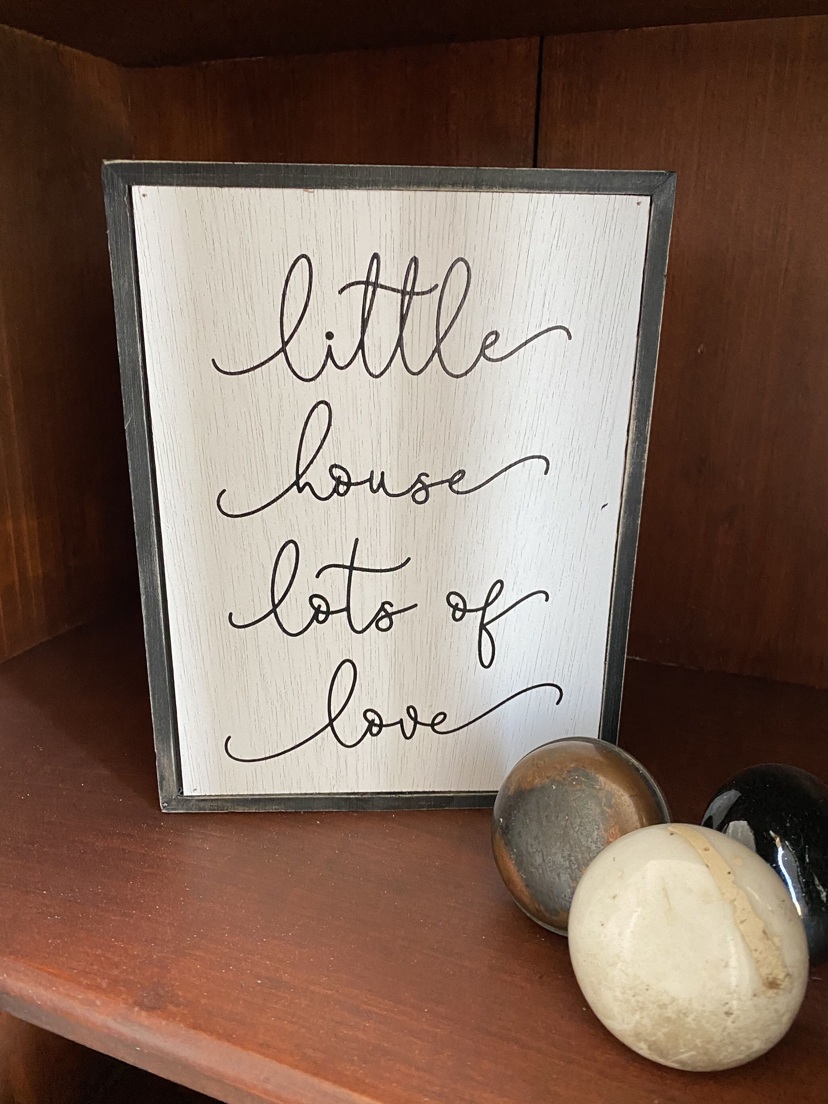 A framed sign with the text "little house lots of love" on a wooden surface.
