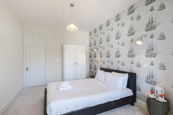 A bedroom with a bed, a wardrobe, a door, and a wall with a ship pattern. - The William IV (London)