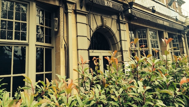 A building with a sign for a bar and restaurant, a lamp post, and a window with a view of the street. - The William IV (London)