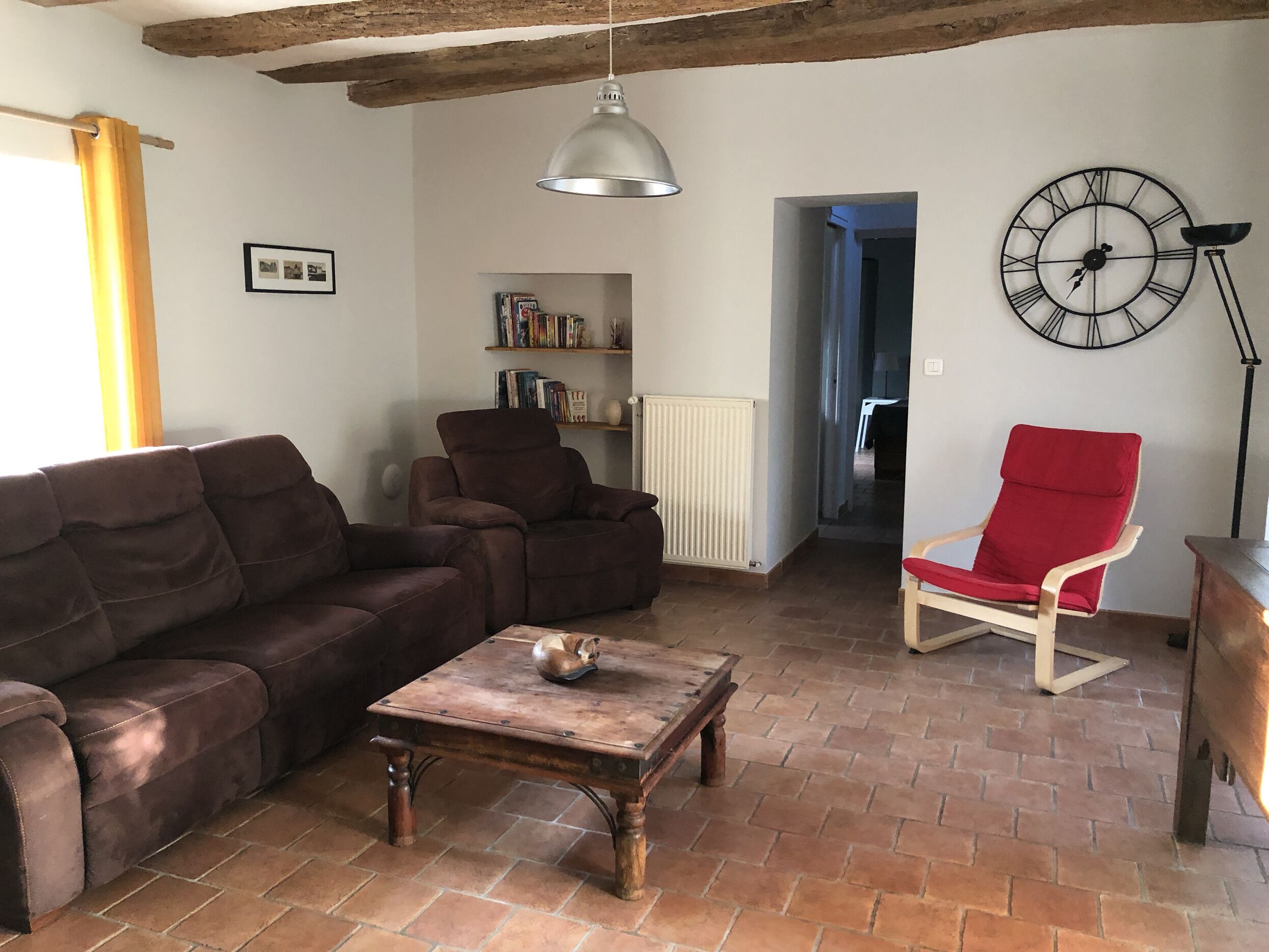 Een woonkamer met een bruine bank, een rode fauteuil, een houten salontafel en een boekenkast.