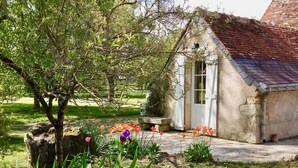 A rustic stone building with a sloped roof, surrounded by a well-maintained garden with various plants and flowers. - Villandry - Domaine de L'augeonnière (Savonnieres)