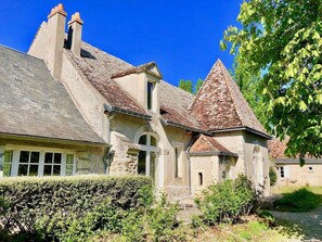 Une maison traditionnelle en pierre, dotée d’un toit à forte pente, d’une cheminée en pierre et d’un petit jardin agrémenté d’une haie et d’un sentier menant à l’entrée.