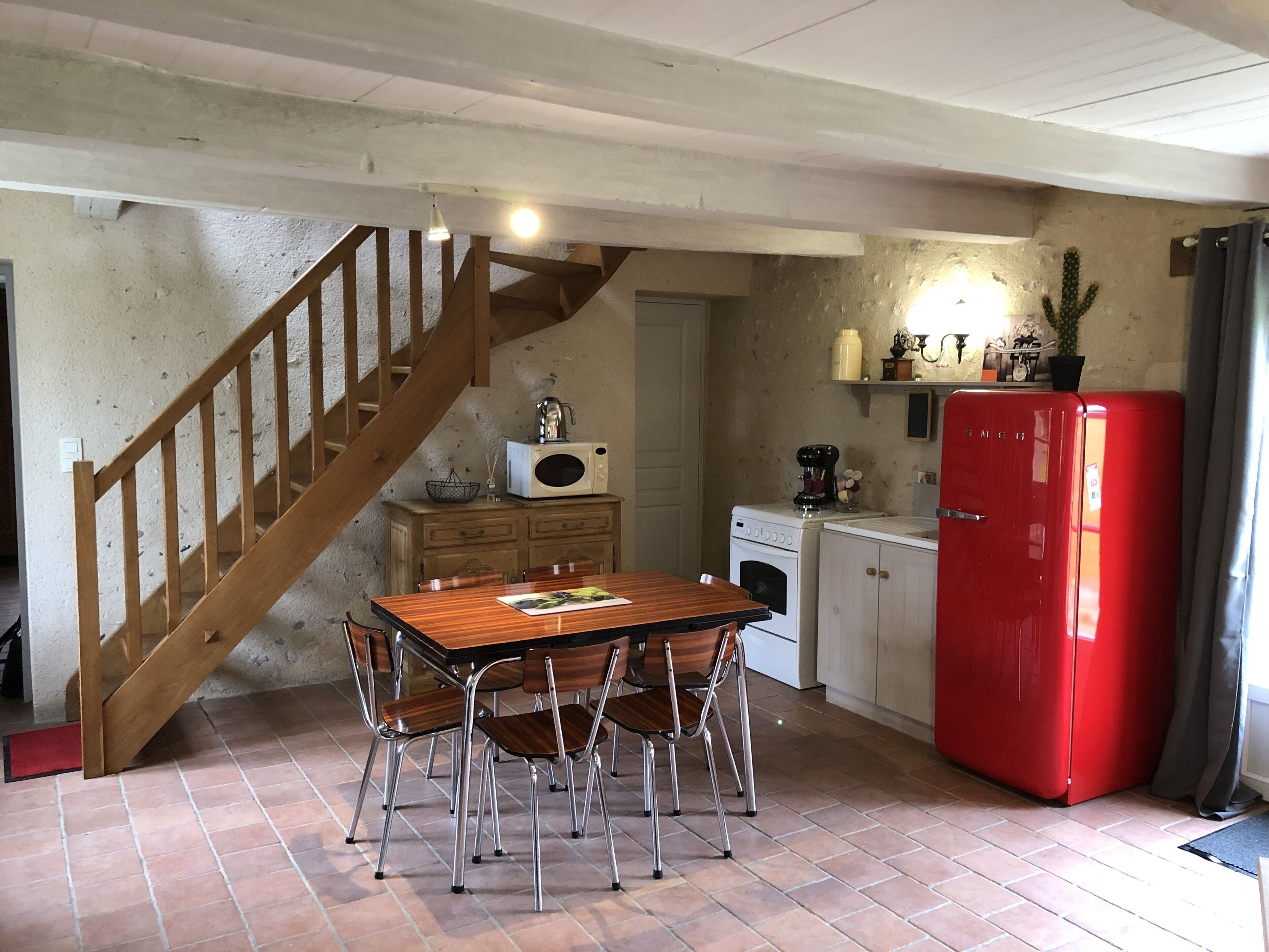 Una cocina con una mesa y sillas de madera, un refrigerador rojo, una cafetera y un microondas sobre un mueble de madera.