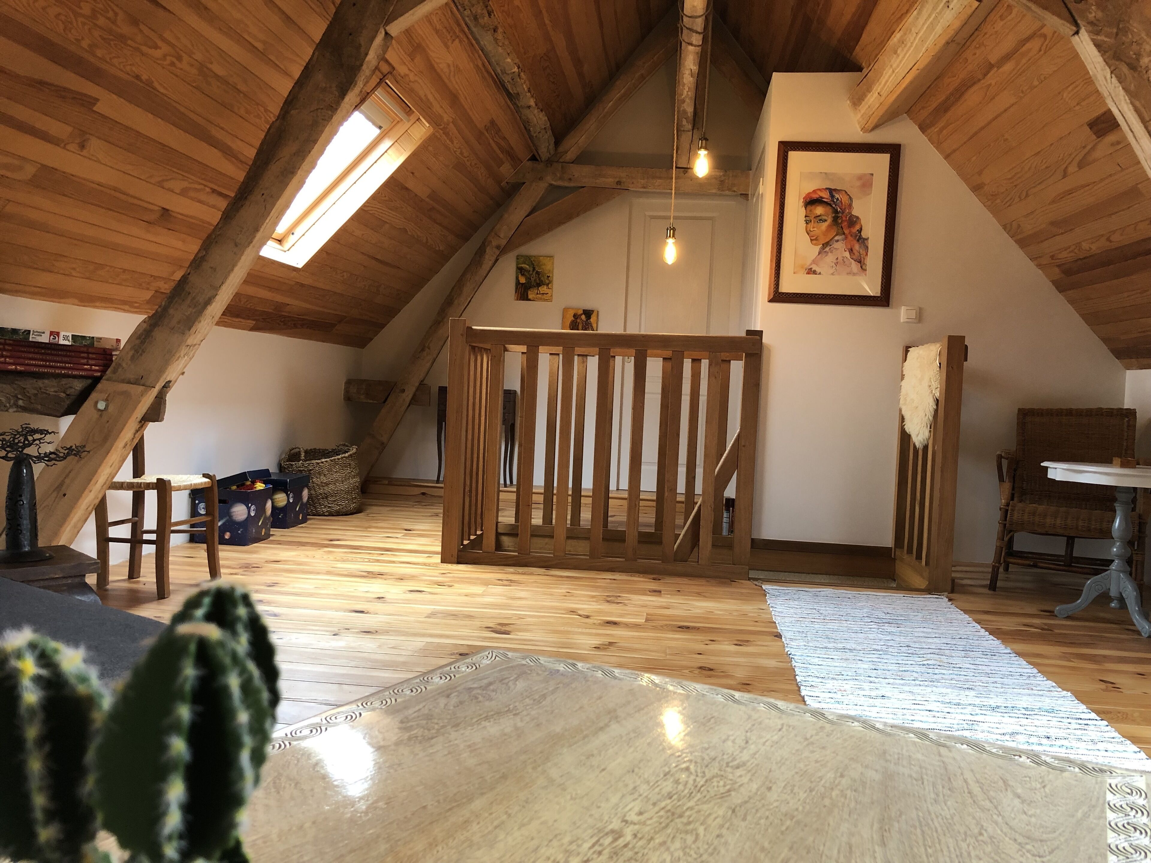Un dormitorio en el ático con vigas de madera, un techo alto, una silla de madera, una mesa y un cuadro en la pared.