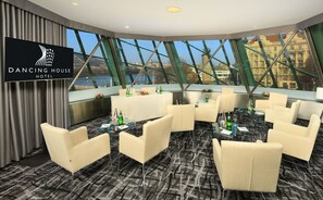 A modern hotel room with a panoramic view of a cityscape through large windows.