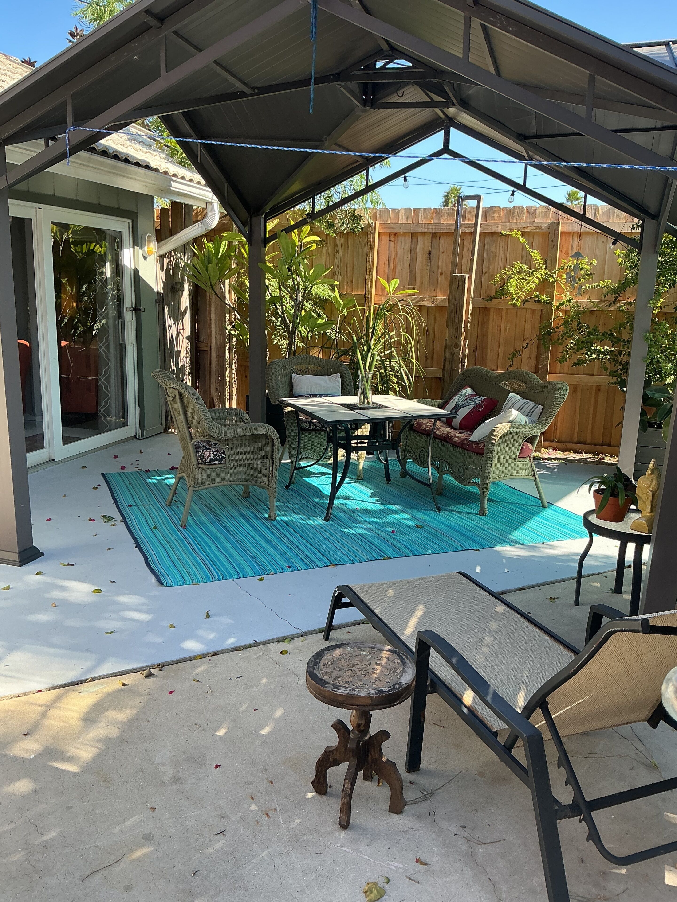 A covered patio with a pool, outdoor furniture, and a wooden fence in the background.