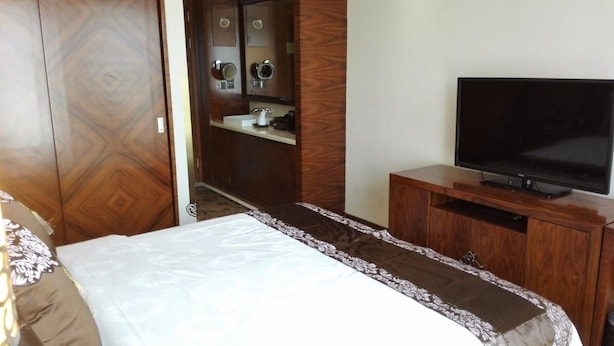 A bedroom with a bed, a TV on a wooden stand, and a bathroom with a sink and mirror. - Inner Mongolia Hotel Forbidden City (Beijing)