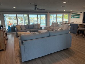 A spacious living room with a large sectional sofa, a dining area, and a view of a pool and waterfront.