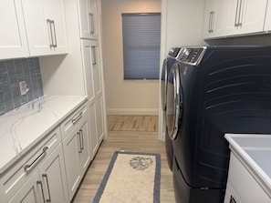 A laundry room with a front-loading washer and dryer, white cabinets, a marble countertop, and a patterned rug. - NEWLY RENOVATED!!! Anna Maria Island - Key Royale - Dock/Lift - Heated Pool/Spa (Holmes Beach)