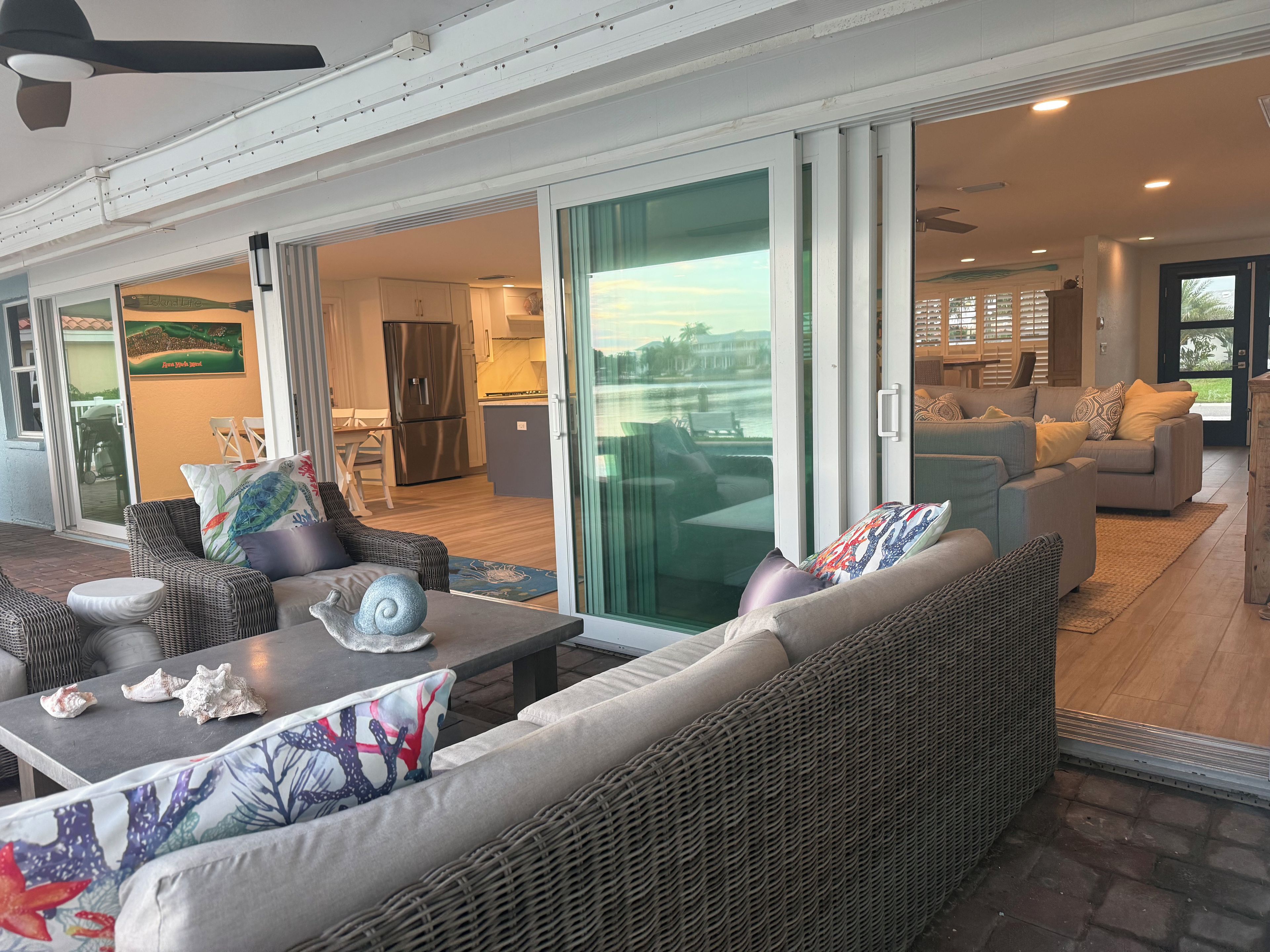 A spacious outdoor seating area with wicker furniture and a view of the kitchen and living room through glass doors.