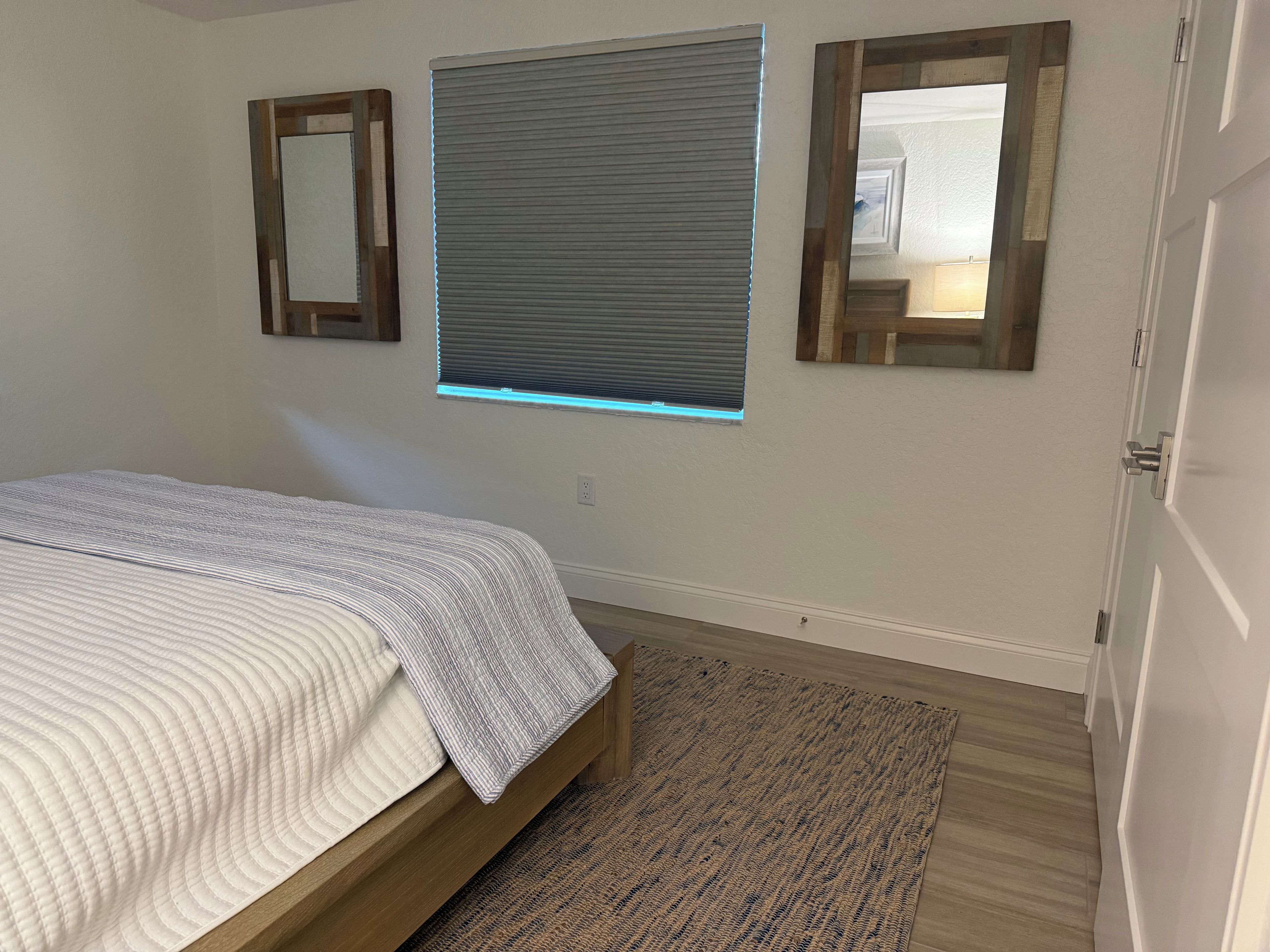 A bedroom with a bed, a window with blinds, and two wall-mounted mirrors.