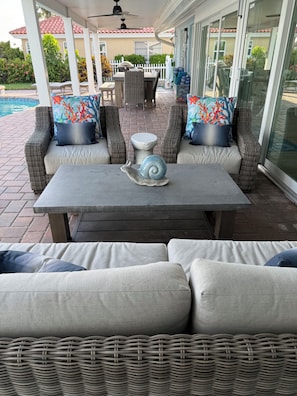 An outdoor patio with wicker furniture, a table with a snail sculpture, and a view of a swimming pool. - NEWLY RENOVATED!!! Anna Maria Island - Key Royale - Dock/Lift - Heated Pool/Spa (Holmes Beach)