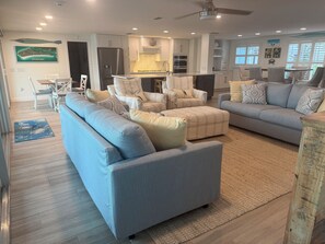 A modern living room with a sofa, ottoman, and chairs, a kitchen area with appliances, and a dining area with a table and chairs.