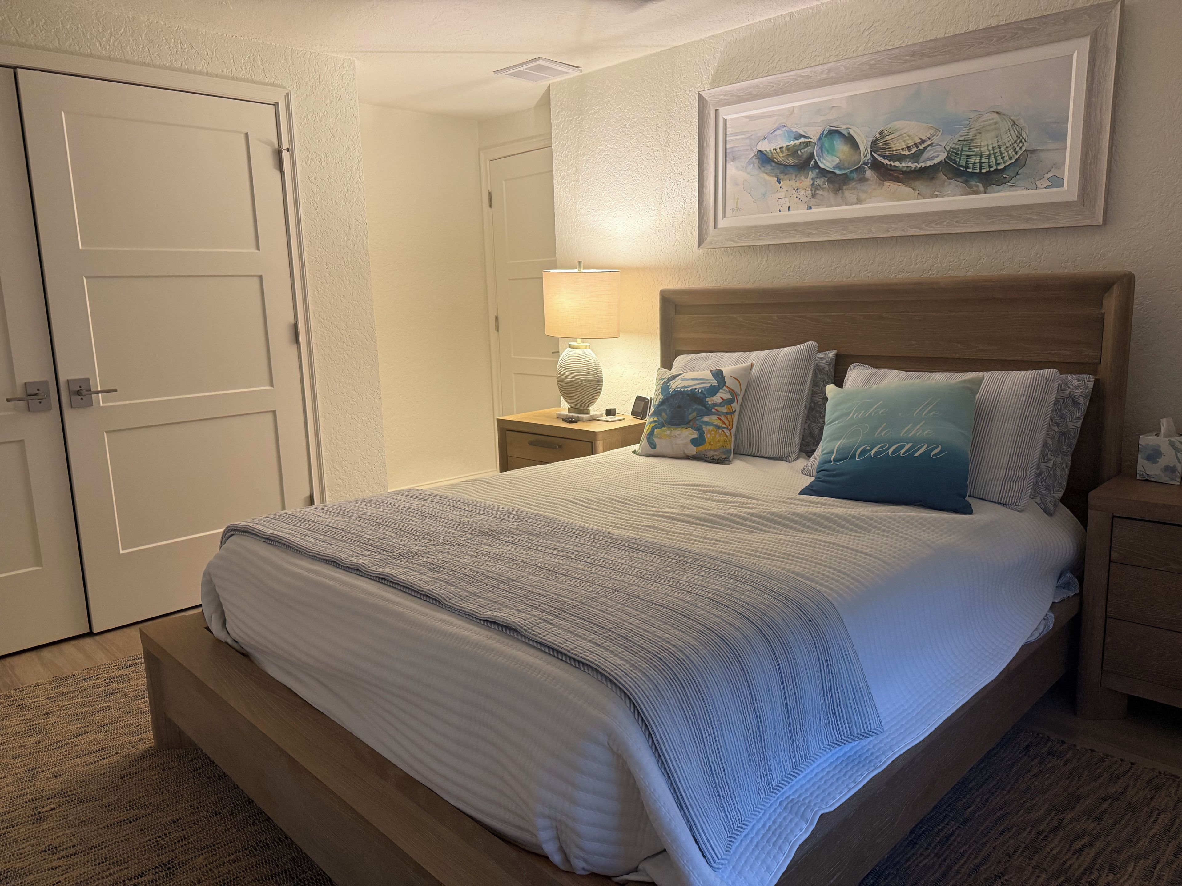 A bedroom with a bed, nightstands, a lamp, and a framed artwork on the wall.