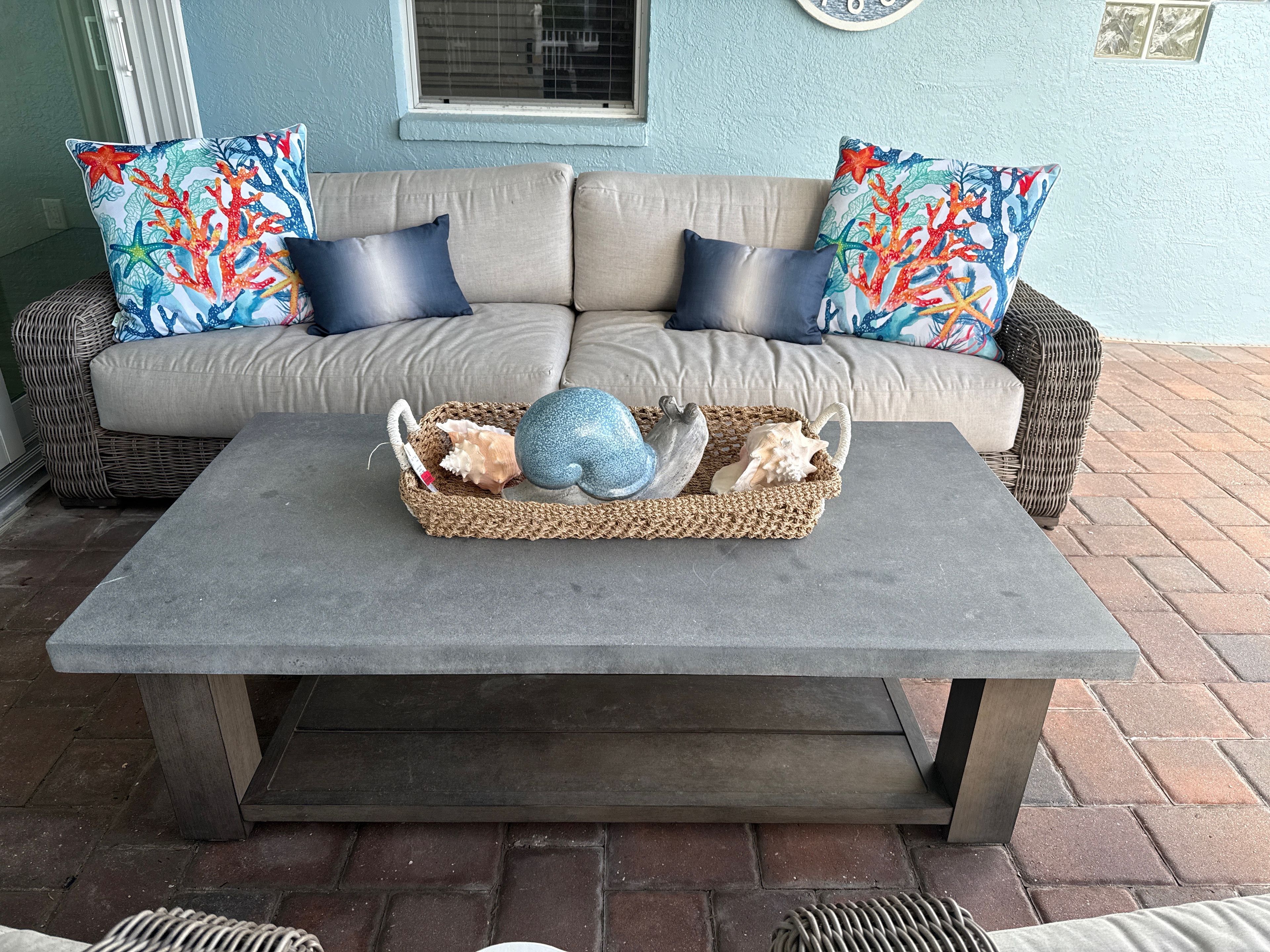 A beige sofa with blue and red patterned pillows, a woven basket with decorative items, and a grey table in a room with a blue wall and window.
