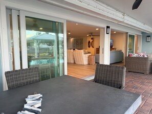 A modern outdoor dining area with a table and chairs, a sliding glass door leading to a patio, and a view of the interior living space.