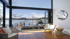 Un balcón amplio con cubierta de madera, una silla de mimbre y vistas a un lago con un muelle y sombrillas.