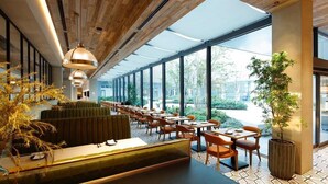 A modern restaurant with a long counter, multiple seating areas, and large windows offering views of the outdoors.