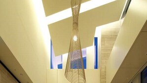A modern lobby with a high ceiling, a unique hanging light fixture, a large window with a city view, and a seating area with sofas and a side table.