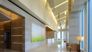 A spacious lobby with a modern design, featuring a large painting, a seating area with a lamp, and a view through large windows.