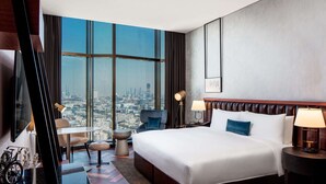 A hotel room with a large bed, a desk, a chair, a TV, and a view of the city.