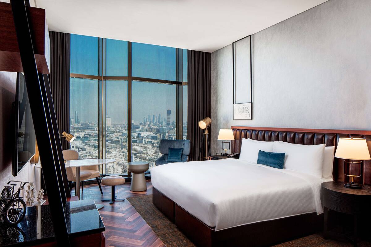 A hotel room with a large bed, a desk, a chair, a TV, and a view of the city.