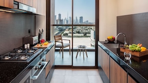 A modern kitchen with a city view, featuring a gas stove, a toaster, and a wooden table with fruits and vegetables.