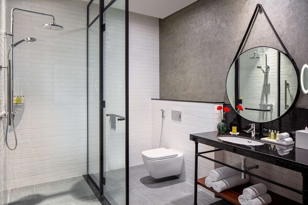 A modern bathroom with a glass shower enclosure, a white toilet, a black sink with a mirror, and a towel rack.