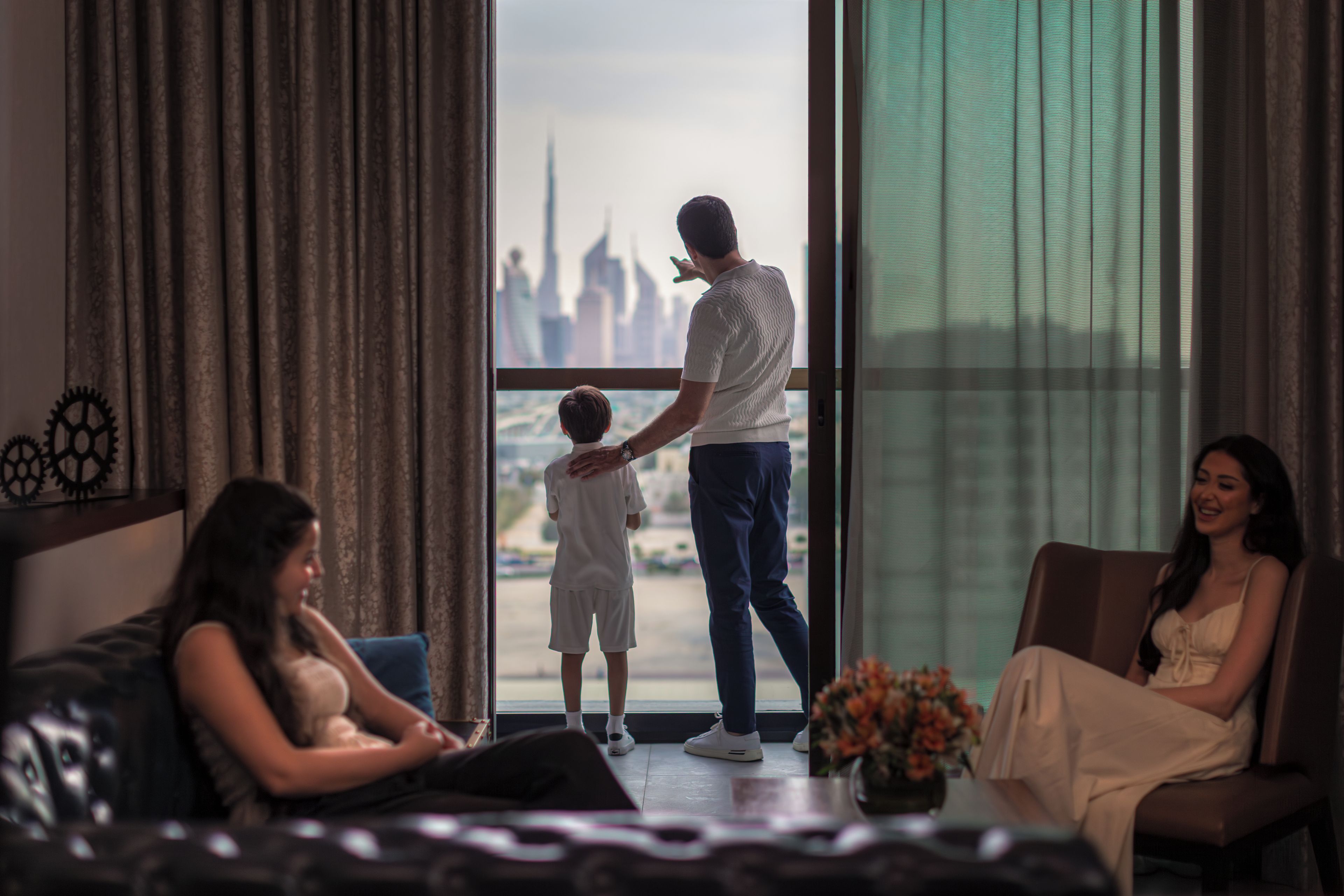 A family in a living room with a city view, a sofa, and a coffee table with flowers.