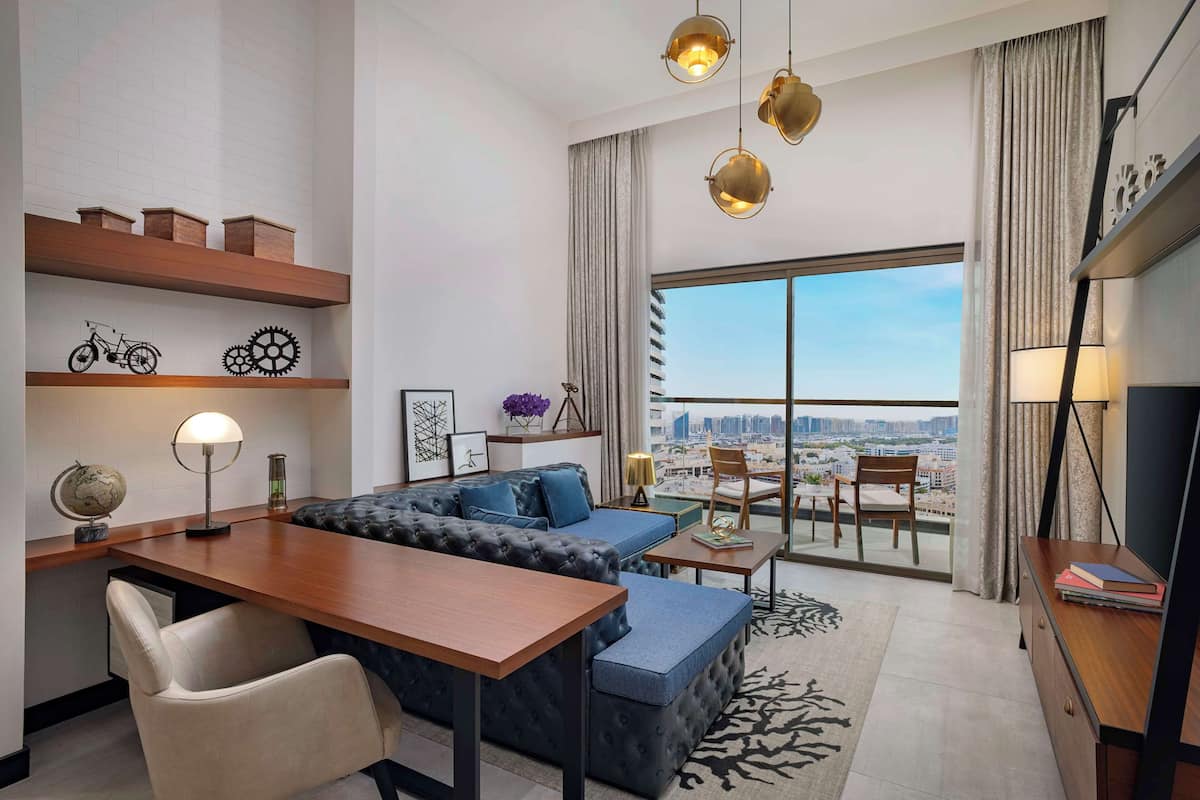 A modern living room with a sofa, a dining table, and a view of a cityscape through large windows.