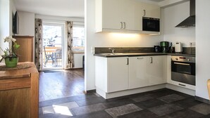 Une cuisine moderne avec des meubles blancs, un four à micro-ondes et un four traditionnel. On aperçoit un coin repas avec une table et des chaises à travers une porte vitrée.