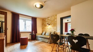 A cozy living area with a stone wall, a wooden floor, a sofa, a dining table with chairs, and a red ottoman. - EVI APARTMENTS - Heike (Kaprun)
