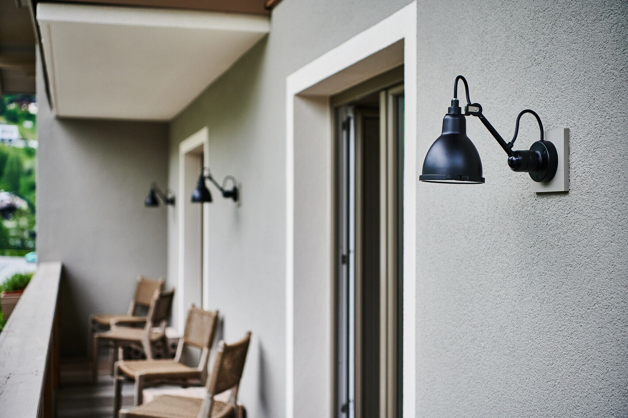 A balcony with wicker chairs and a wall-mounted lamp.