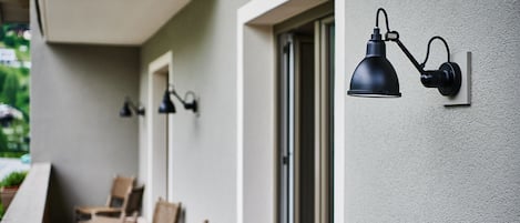 A balcony with wicker chairs and a wall-mounted lamp.