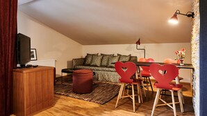 Een gezellig loft-appartement met hoge plafonds, een donker houten bureau, een rode stoel in de vorm van een hart, een zwarte televisie en een eethoek met een rode tafel en bijpassende stoelen.
