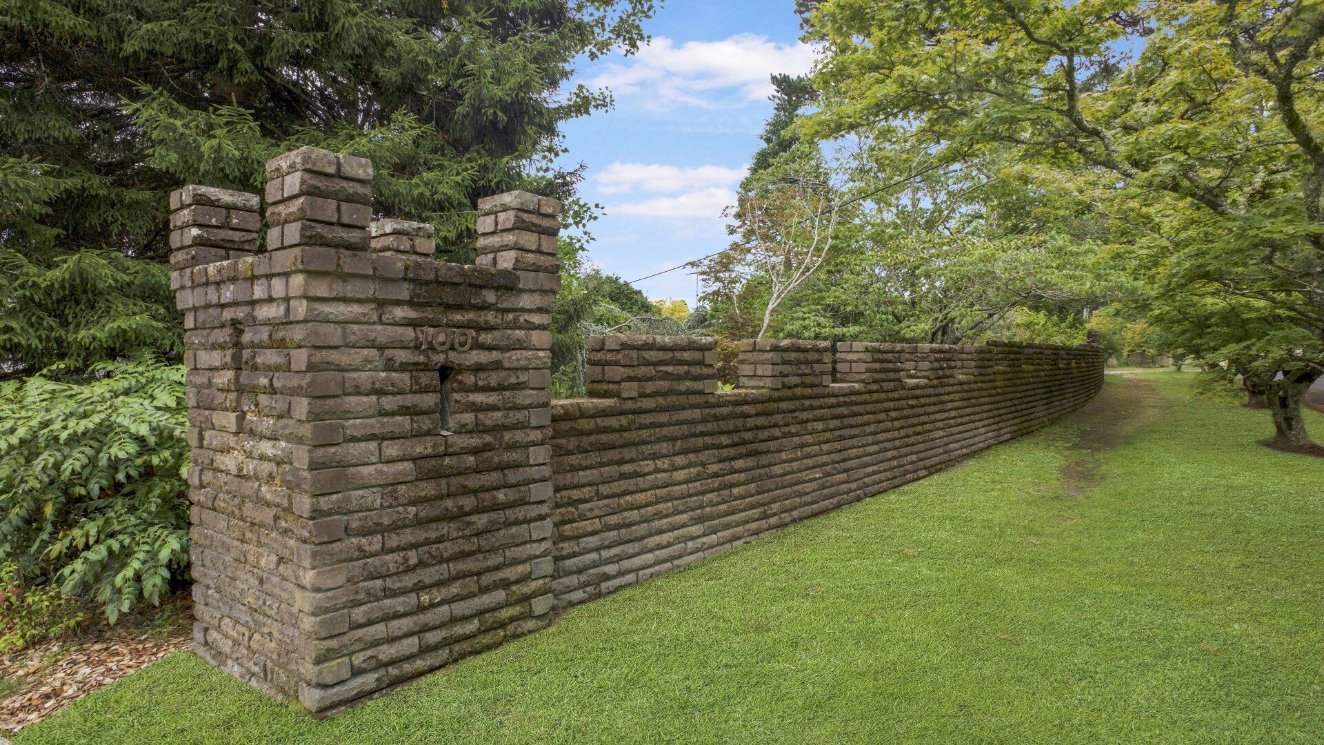 A stone wall with a number '100' on it, surrounded by grass and trees.