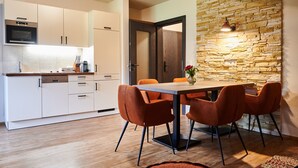 A modern kitchen with white cabinets, a built-in oven, and a dining area with a wooden table and orange chairs. - EVI APARTMENTS - Valerie (Kaprun)