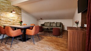 A modern living room with a stone accent wall, a dining area with orange chairs, a sofa with patterned cushions, and a wooden coffee table. - EVI APARTMENTS - Valerie (Kaprun)