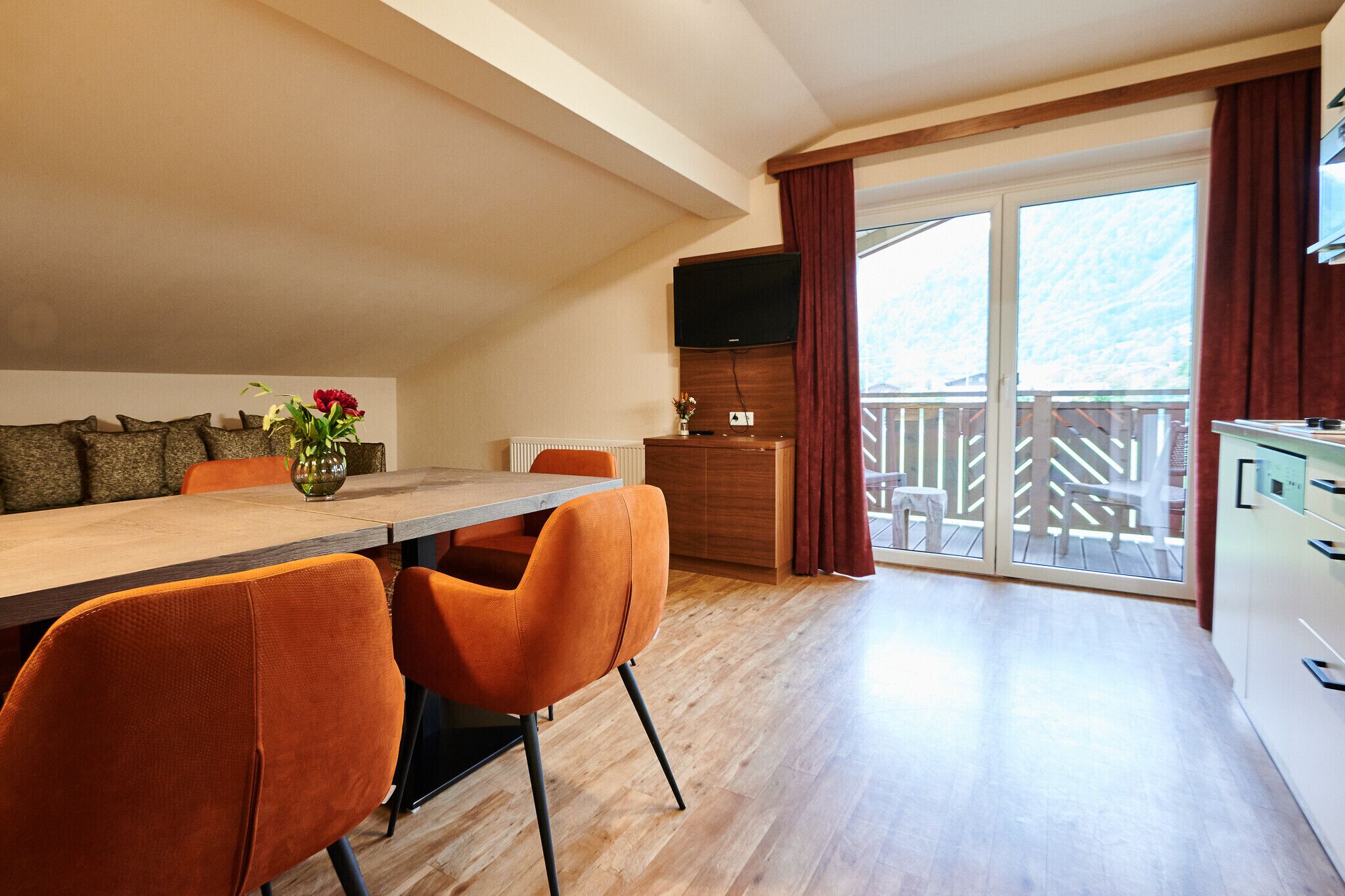 A modern kitchen with a wooden countertop, a dining area with orange chairs, and a large sliding glass door leading to a balcony.