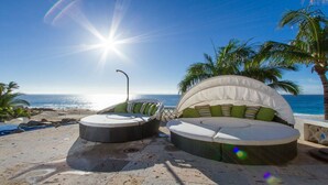 Een strandlounge met uitzicht op de oceaan, met een rond zitgedeelte en een halvemaanvormige bank met kussens.